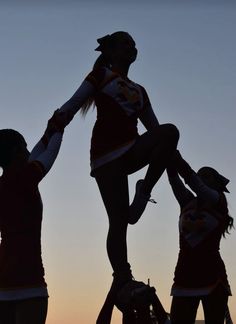 the silhouette of three cheerleaders are holding their hands in the air as the sun sets