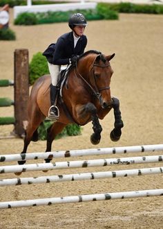 a woman riding on the back of a brown horse while jumping over a white fence