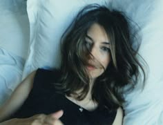 a woman laying in bed with her hand on the pillow and pointing at something she is holding