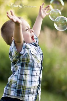 a young boy is playing with bubbles in the air and has his hands out to catch it