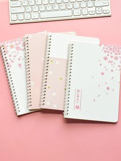 three notebooks sitting next to a keyboard on top of a pink surface with flowers