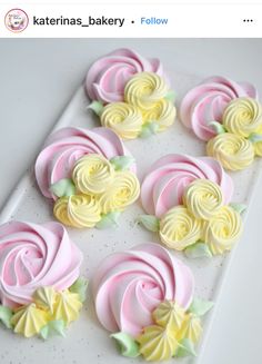 some pink and yellow cupcakes are on a white platter with green leaves