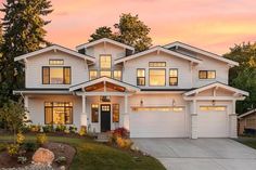 a large white house with lots of windows and trees in the front yard at sunset