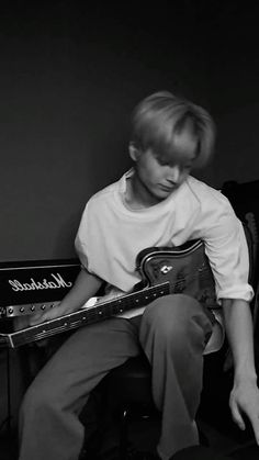 a young man sitting in a chair playing an electric guitar