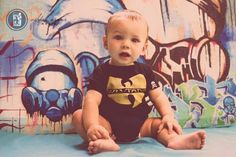 a baby sitting in front of a wall with graffiti on it's walls and looking at the camera