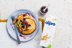 a plate with pancakes and berries on it next to a carton of almond milk