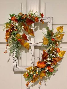 a wreath hanging on the side of a door with autumn leaves and flowers around it