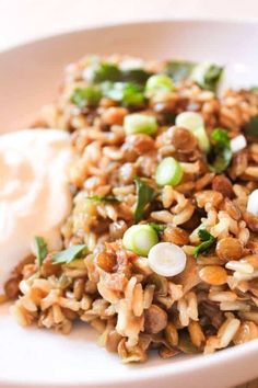 a white plate topped with rice and veggies next to sour cream on a table