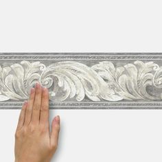 a hand is reaching up to the edge of a decorative wallpaper border with an intricate design