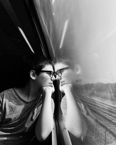 a young man wearing glasses looking out the window on a train or subway car, in black and white