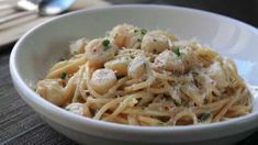 a white bowl filled with pasta covered in shrimp and parmesan cheese on top of a wooden table