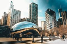 people are standing in front of a large shiny ball on the ground with skyscrapers in the background