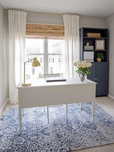 a white desk sitting in front of a window next to a blue rug on top of a wooden floor