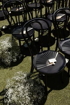 many black chairs and tables on grass with white flowers in the backgroung