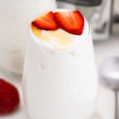 a glass filled with yogurt and topped with strawberries next to a blender