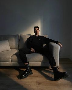 a man sitting on top of a couch next to a white wall and wooden floor