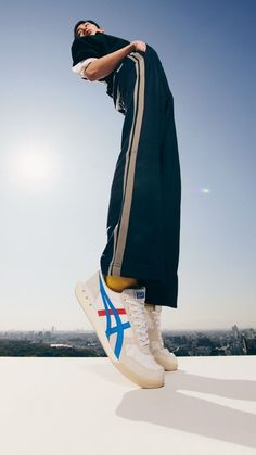 a man standing on top of a roof with his feet in the air and wearing white sneakers