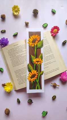 an open book sitting on top of a table filled with flowers and leaves next to petals