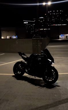 a black motorcycle parked in an empty parking lot at night with city lights behind it