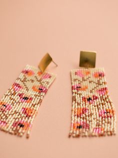 a pair of beaded earrings sitting on top of a pink table next to each other