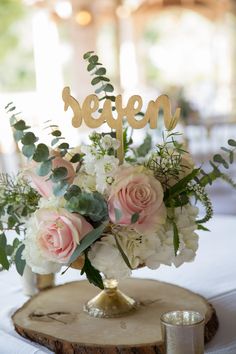 a centerpiece with flowers and greenery is displayed on a wooden slice at the head table