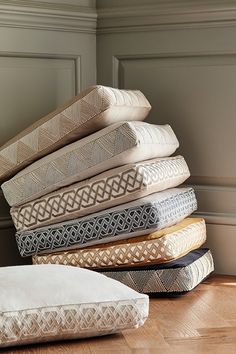 a stack of pillows sitting on top of a hard wood floor next to a wall