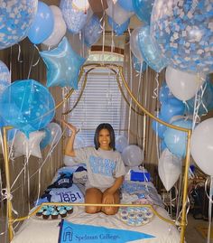 a woman sitting on a bed surrounded by blue and white balloons