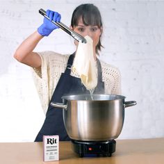 a woman in an apron and blue gloves is stirring a pot