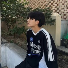 a young man sitting on top of a cement step next to a tree and building