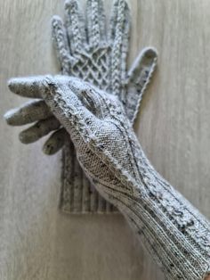 a pair of gray knitted gloves sitting on top of a wooden table next to a white wall