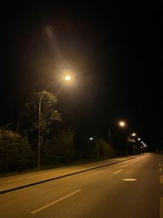 an empty road at night with street lights and trees on both sides, in the dark