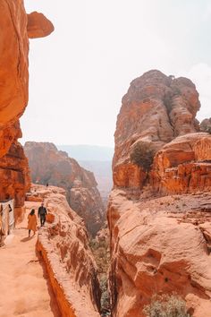 two people are walking along a narrow path in the middle of some rocks and sand