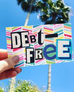 a person holding up a sticker with the words debt free written in multicolored letters