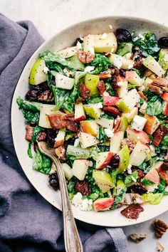 a white bowl filled with salad next to a gray napkin and silver spoon on top of a table