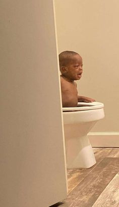 a baby sitting on top of a toilet in a bathroom next to an open door