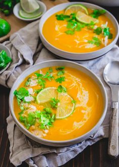 two bowls filled with soup and garnished with cilantro, parsley and lime