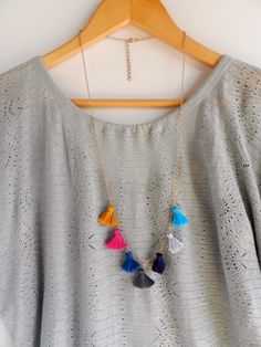 a gray sweater with colorful tassels hanging on a wooden hanger next to a white wall