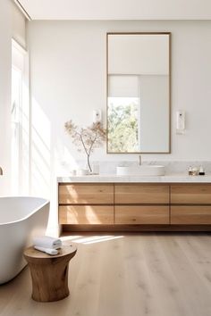 a white bath tub sitting next to a large mirror on top of a wooden cabinet