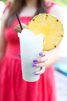 a woman in a red dress holding a pineapple drink