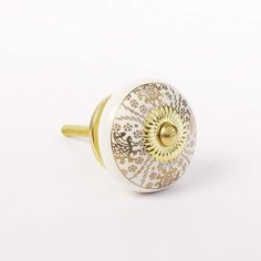 a white and gold door knob with an intricate design on the front, sitting on a white surface