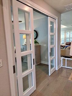 an open door leading to a living room and dining area with wood floors, white walls and glass doors