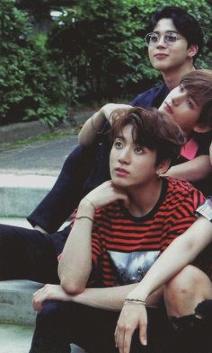 three young men sitting on the steps in front of some trees and bushes with their arms around each other