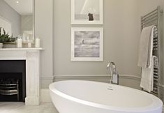 a white bath tub sitting next to a fire place in a living room with pictures on the wall