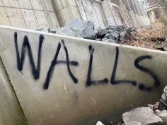 graffiti writing on the side of a wall next to some rocks and trees in front of a building