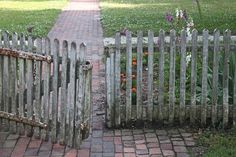 an old wooden fence with flowers growing between it and a brick path in the background