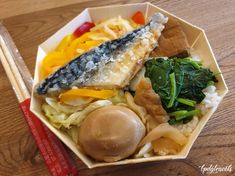 a bowl filled with rice, fish and vegetables next to chopsticks on a wooden table