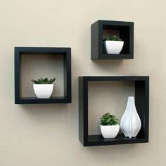 three square black shelves with white vases and plants on them against a beige wall