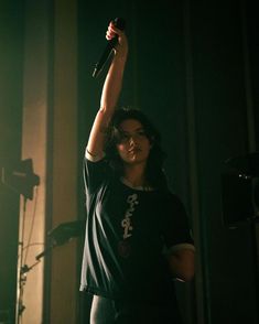 a woman holding a microphone up in the air with her hand raised above her head