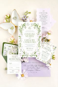 the wedding stationery is laid out on top of each other with flowers and greenery