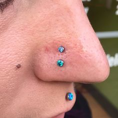 a woman's nose with blue and green piercings on her left side ear